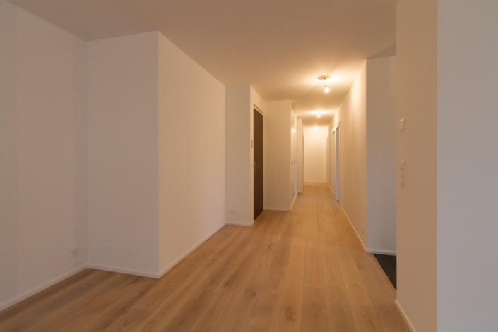 Couloir traversant avec murs neufs blancs et parquet au sol