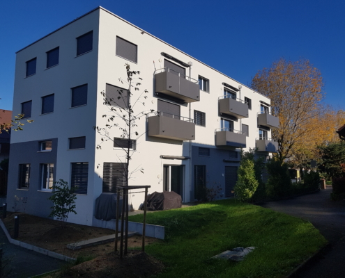 Tolochenaz projet Minergie logements - photo en contre plongée d'un immeuble à Tolochenaz récent gris et blanc avec petits balcons et ciel bleu