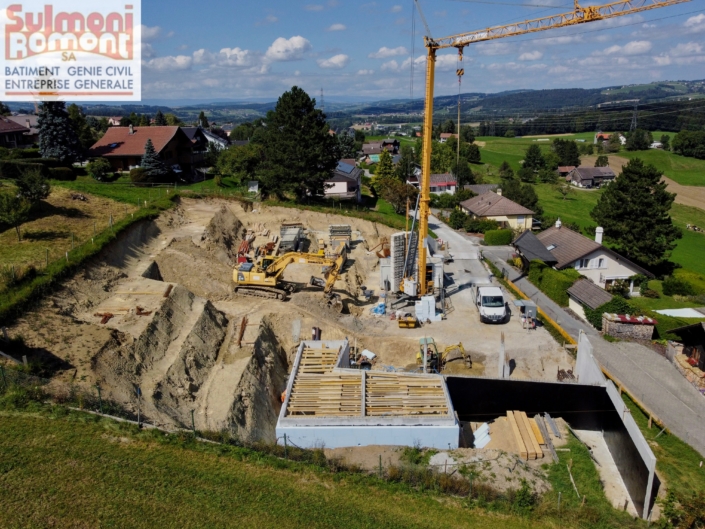 image prise par un drôle du chantier de la promotion à Granges Veveyse "La Dent-de-Lys" avec terrain creusé entourép de verdure et grue jaune au centre de l'image