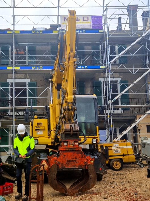 Directeur de travaux se tenant devant un immeuble en démolition avec des échafaudages et des machines de chantier